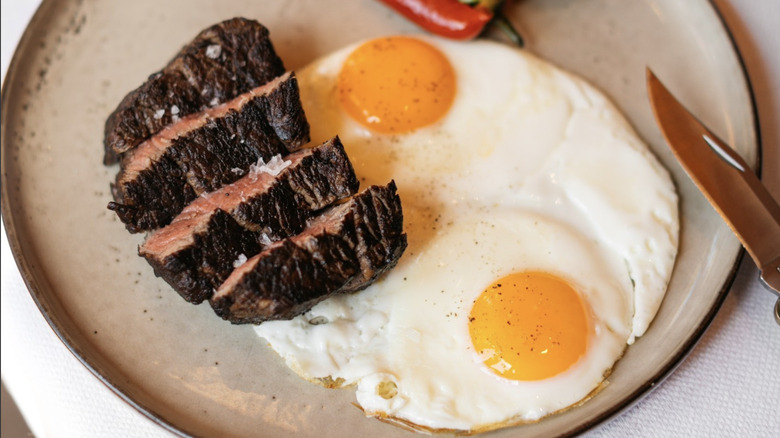 Steak and eggs on white plate with knife