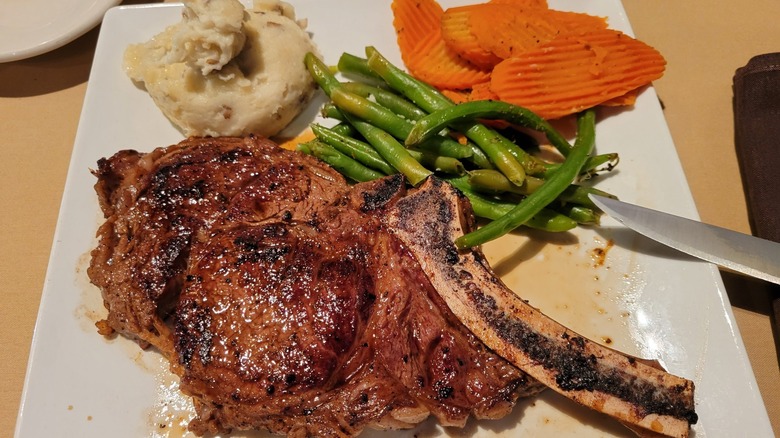 bone-in steak with green beans, carrots and mashed potato on white plate