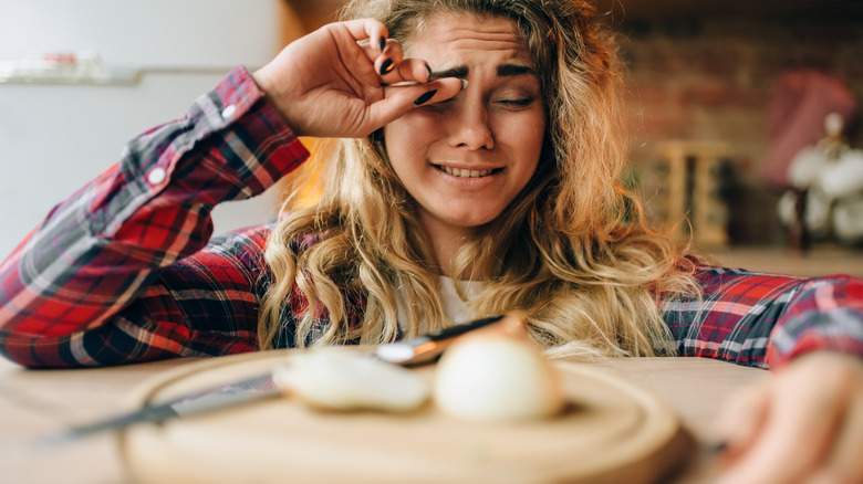 woman rubbing eye with onion and knife