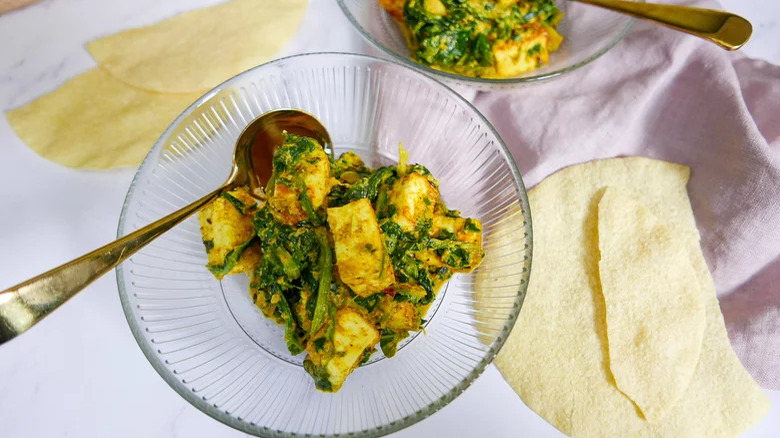 bowls of saag paneer with papadum and spoons