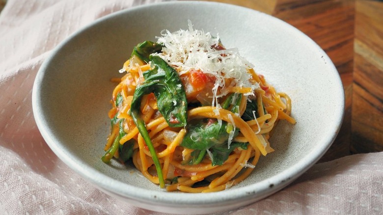 bowl of pasta with spinach and tomatoes with cheese on top