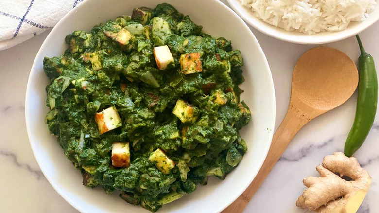 bowl of palak paneer with wooden spoon and white rice