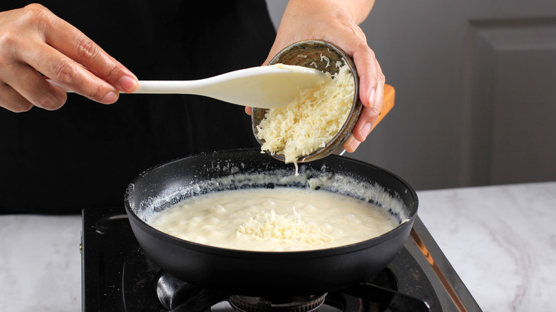 grated cheese and sauce with hands and spoon