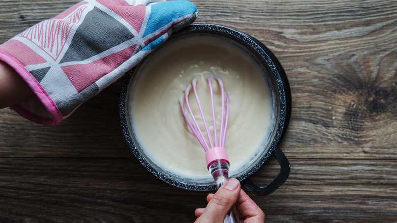 sauce in pan with whisk and oven glove