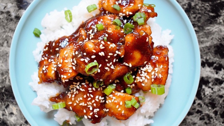 Sesame chicken on rice with scallion garnish