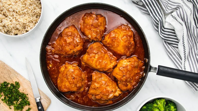 Chicken thighs in sauce in skillet with rice