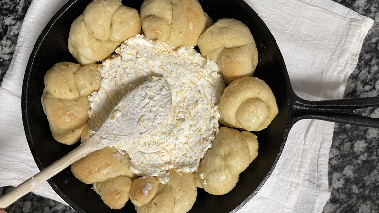 bread knots, cheese, and a wooden spatula in a black frying pan