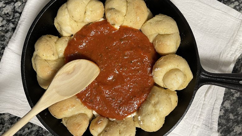 bread knots, tomato sauce, and a wooden spatula in a black frying pan