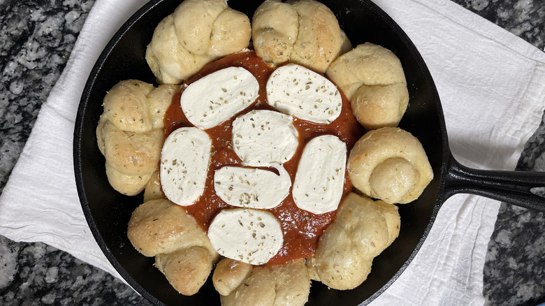 bread knots, cheese, and tomato sauce in a black frying pan