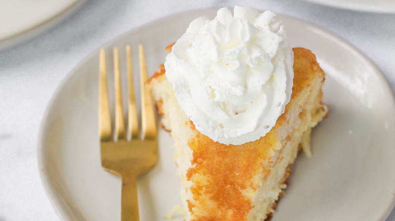 Close up of a slice of angel food cake topped with whipped cream next to a fork