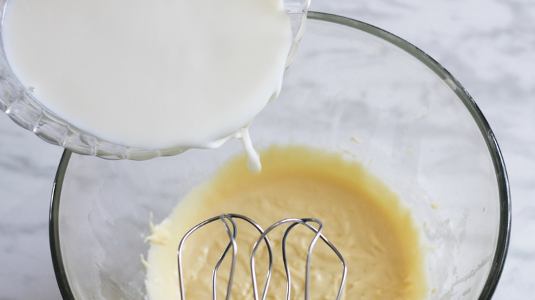 adding batter to egg yolks in bowl with blender whisks