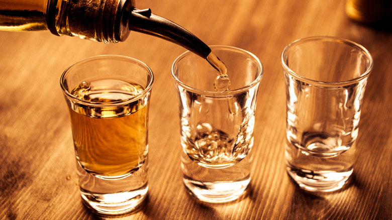 three shot glasses on a bar being filled up