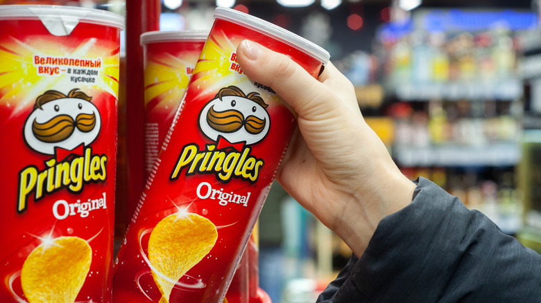 Person grabbing a can of Original Pringles off the shelf