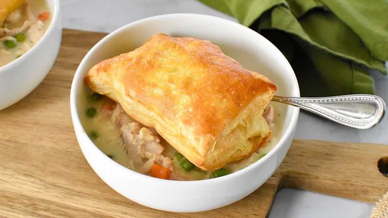 Bowl of chicken, veggies and gravy with puff pastry topping.