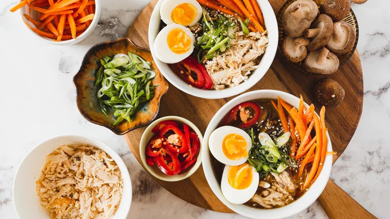 Bowls of broth, chicken, hard-cooked eggs, and sliced vegetables.