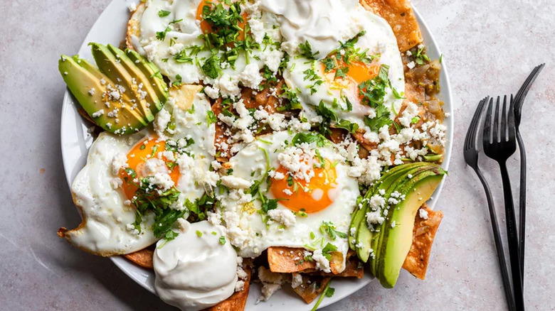 Plate with tortilla chips. fried eggs, avocado, and herbs. 