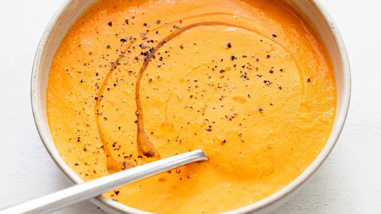 Bowl of creamy, orange soup with cracked black pepper and oil. 