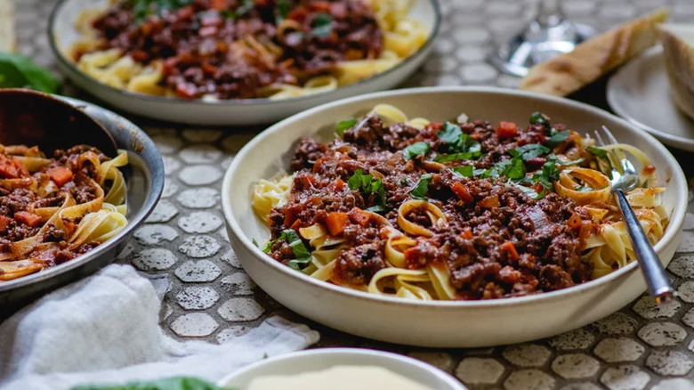 Plates with noodles and beef-carrot sauce, topped with herbs.