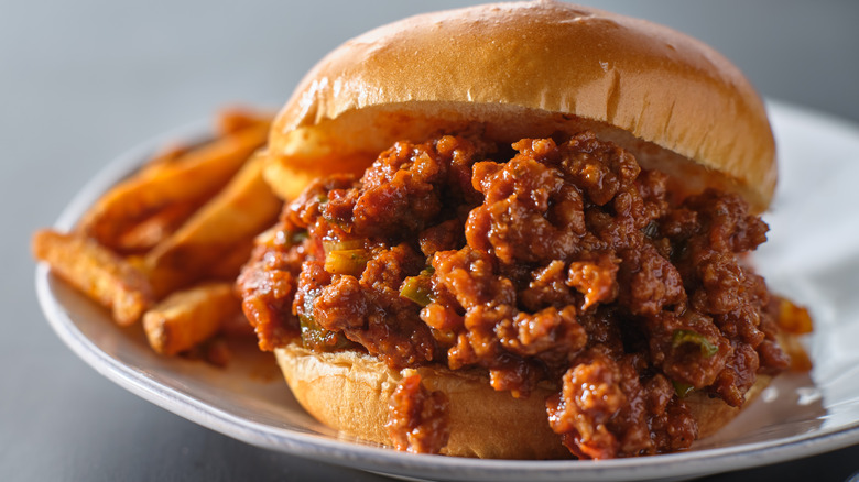 Sloppy joe beef and sauce mixture on burger bun with fries.