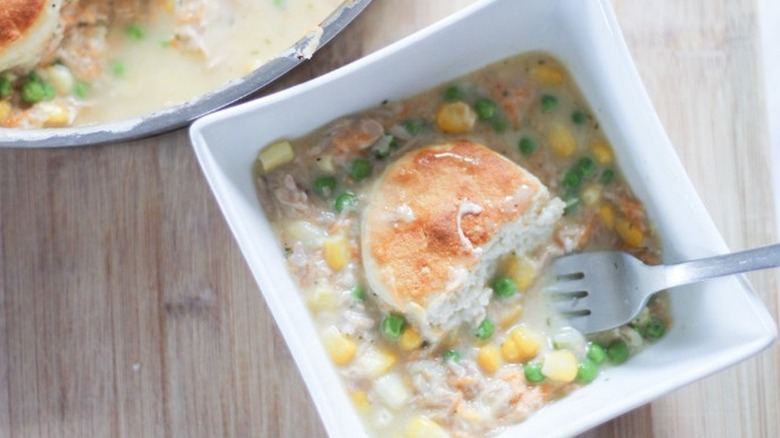 Square dish of tuna casserole with veggies topped with biscuit.