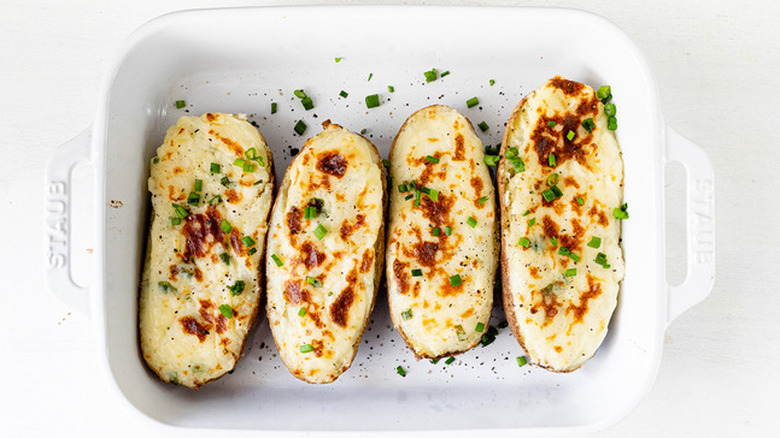 Four potato halves in baking dish with melted cheese and scallions.