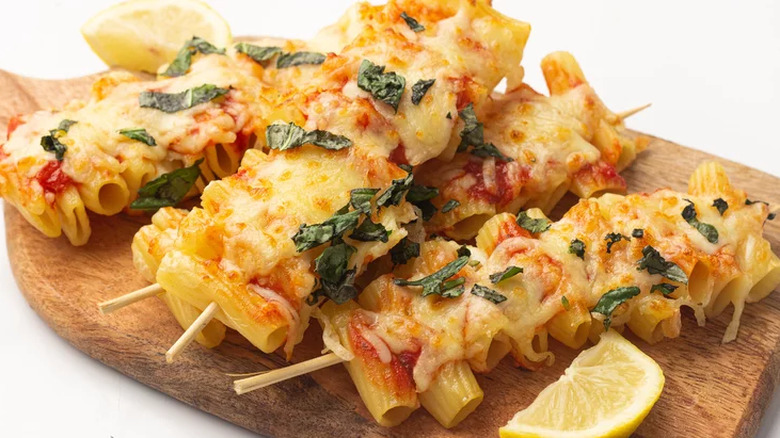 Wood skewers with cooked pasta, melted cheese, and sauce.