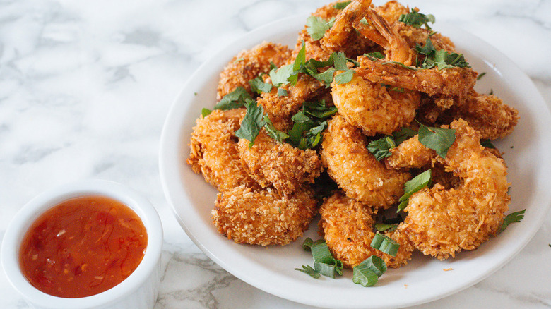 White plate with pile of crispy breaded shrimp and parsley..