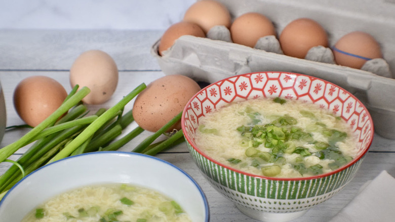 Bowls of egg drop soup near carton of whole eggs.