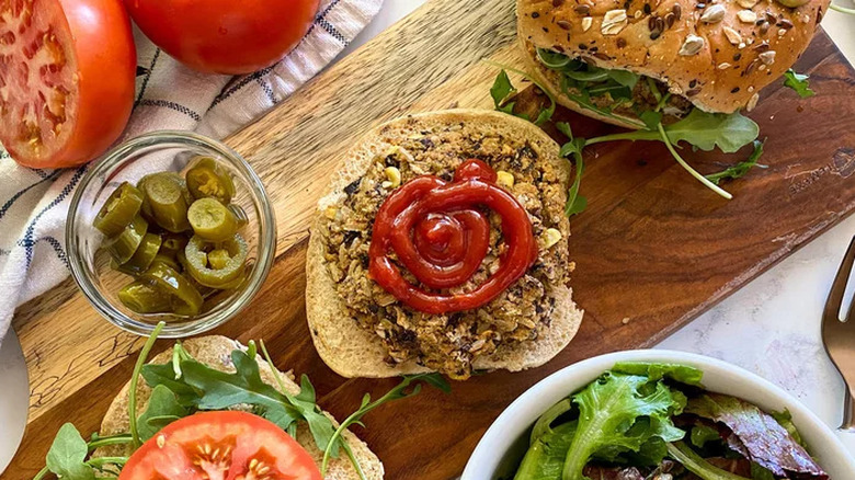 Bean and rice burger on bun with ketchup, with veggies nearby.