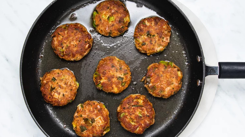 Browned patties of tuna and scallions in a dark frying pan. 