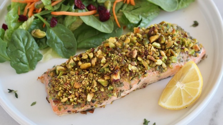 Slice of salmon topped with chopped pistachios on a plate.