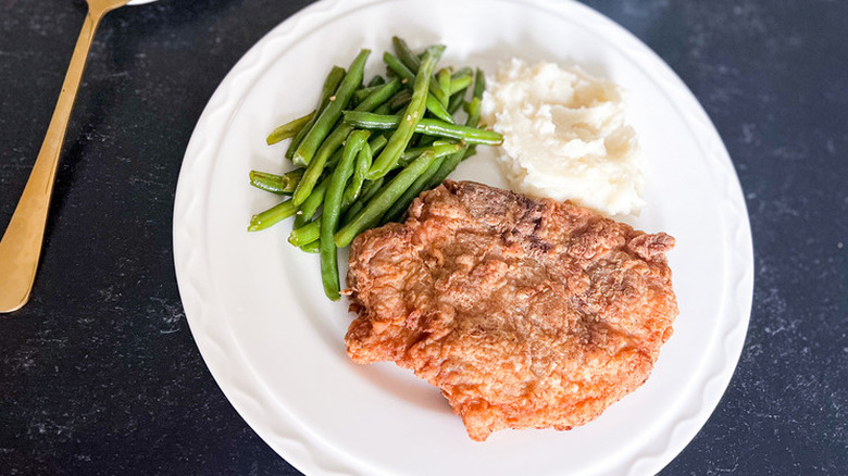 Fried pork chop on a plate with beans and potatoes.