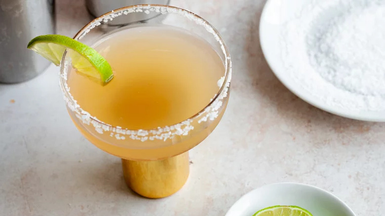 Orange-colored margarita with salt rim and lime slice.