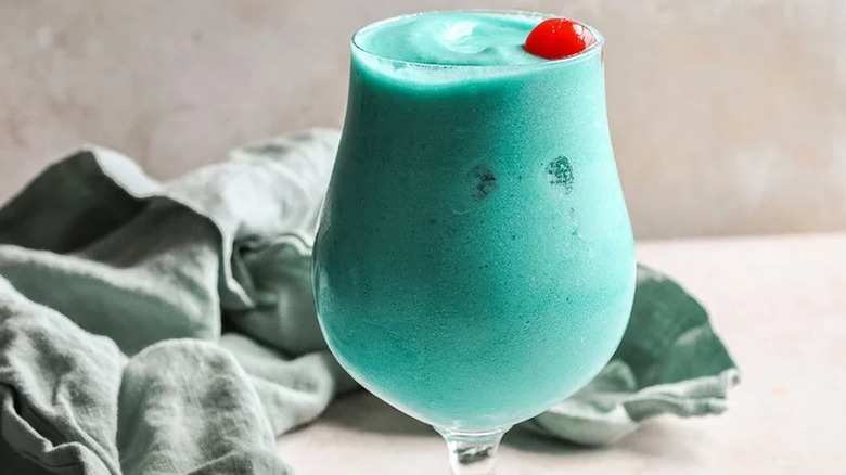 Frozen blue cocktail in glass with cherry.