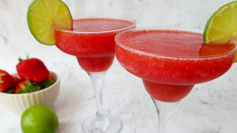 Tall cocktail glasses with frozen strawberry daiquiri and lime. 