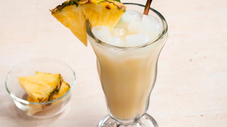 Milkshake glass with creamy yellow drink and fresh pineapple.