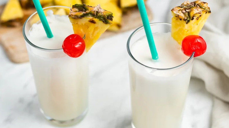 Two glasses with creamy coconut drinks garnished with pineapple.