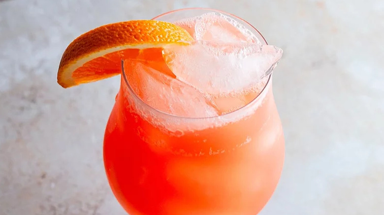 Cocktail glass with reddish-orange drink and orange slice.