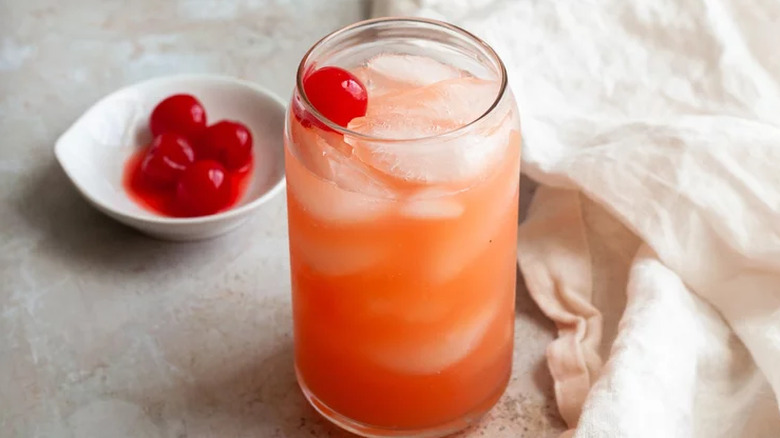 Tall glass with red-orange cocktail over ice.