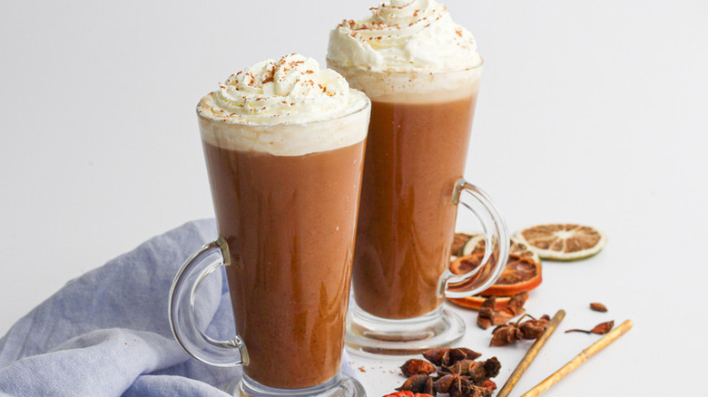 Two tall glass mugs of pumpkin latte with whipped cream.