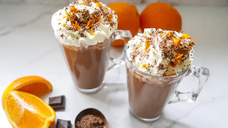 Two tall mugs of hot chocolate with cream and orange