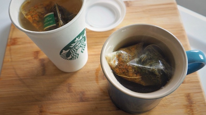 Hot tea drinks in a mug and a white Starbucks cup.