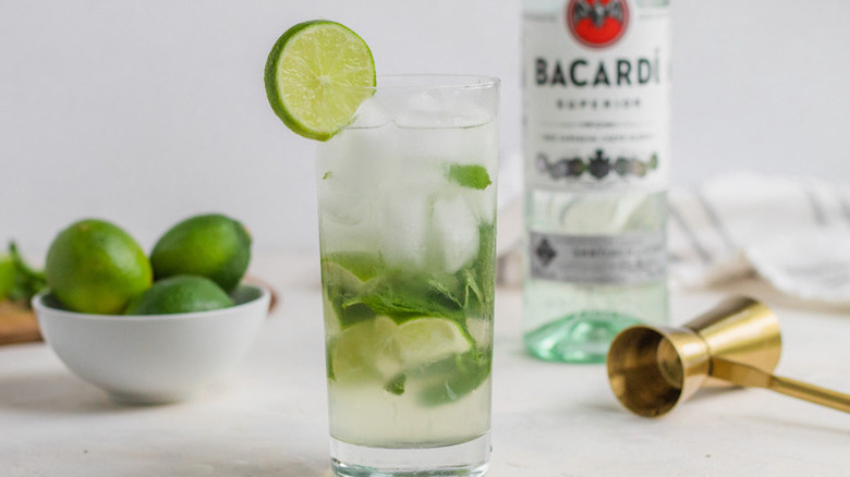 Tall glass with lime, rum, ice, and mint leaves. 