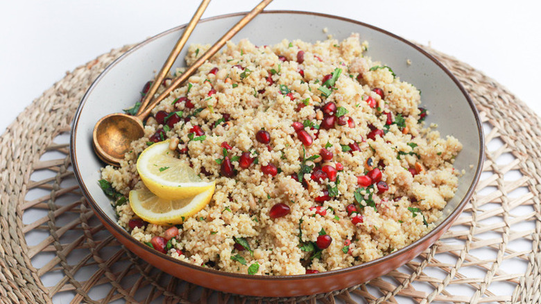 Bowl of couscous with pomegranate seeds and diced green herbs.