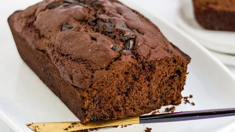 Loaf of chocolate banana bread with knife on platter.