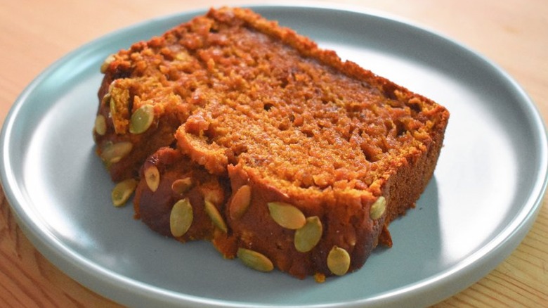 Slice of orange pumpkin bread with pumpkin seeds. 