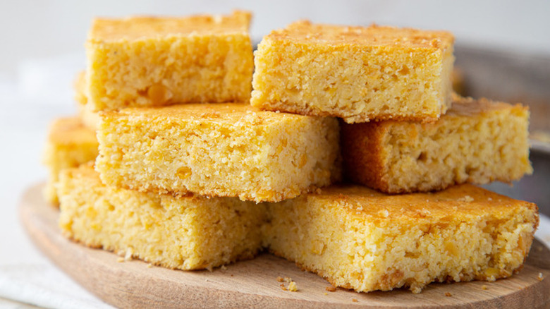 Squares of cornbread and crumbs on a cutting board.