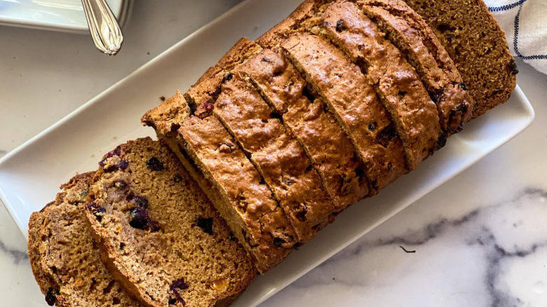 Sliced loaf of fruit-studded bread on platter.