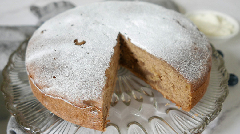 Round, sugar-dusted banana bread loaf with slice out. 