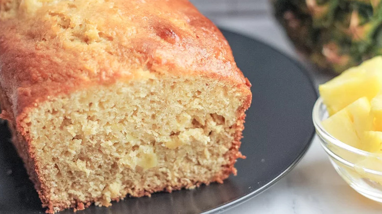 Sliced open loaf of pineapple bread on dark plate. 